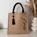Sac en Toile de Jute avec Pompon Noir et Personnalisé avec Prénom en Calligraphie Arabe sur le coter