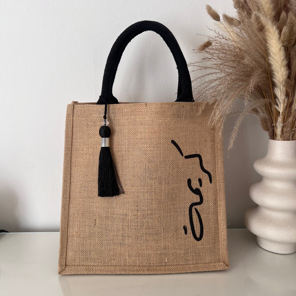 Sac en Toile de Jute avec Pompon Noir et Personnalisé avec Prénom en Calligraphie Arabe sur le coter